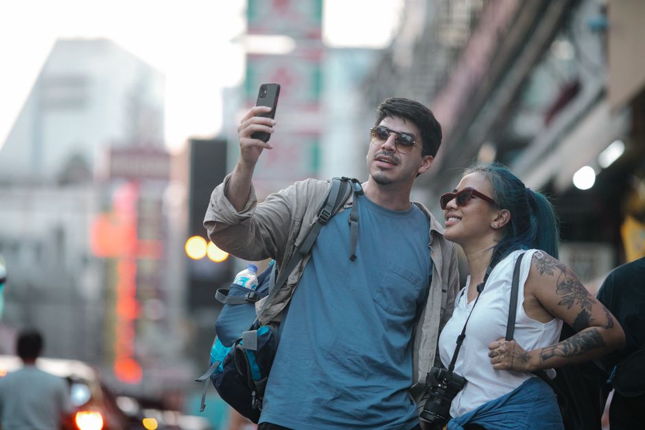 Smiling couple capturing a selfie on a busy city street, enjoying travel moments.